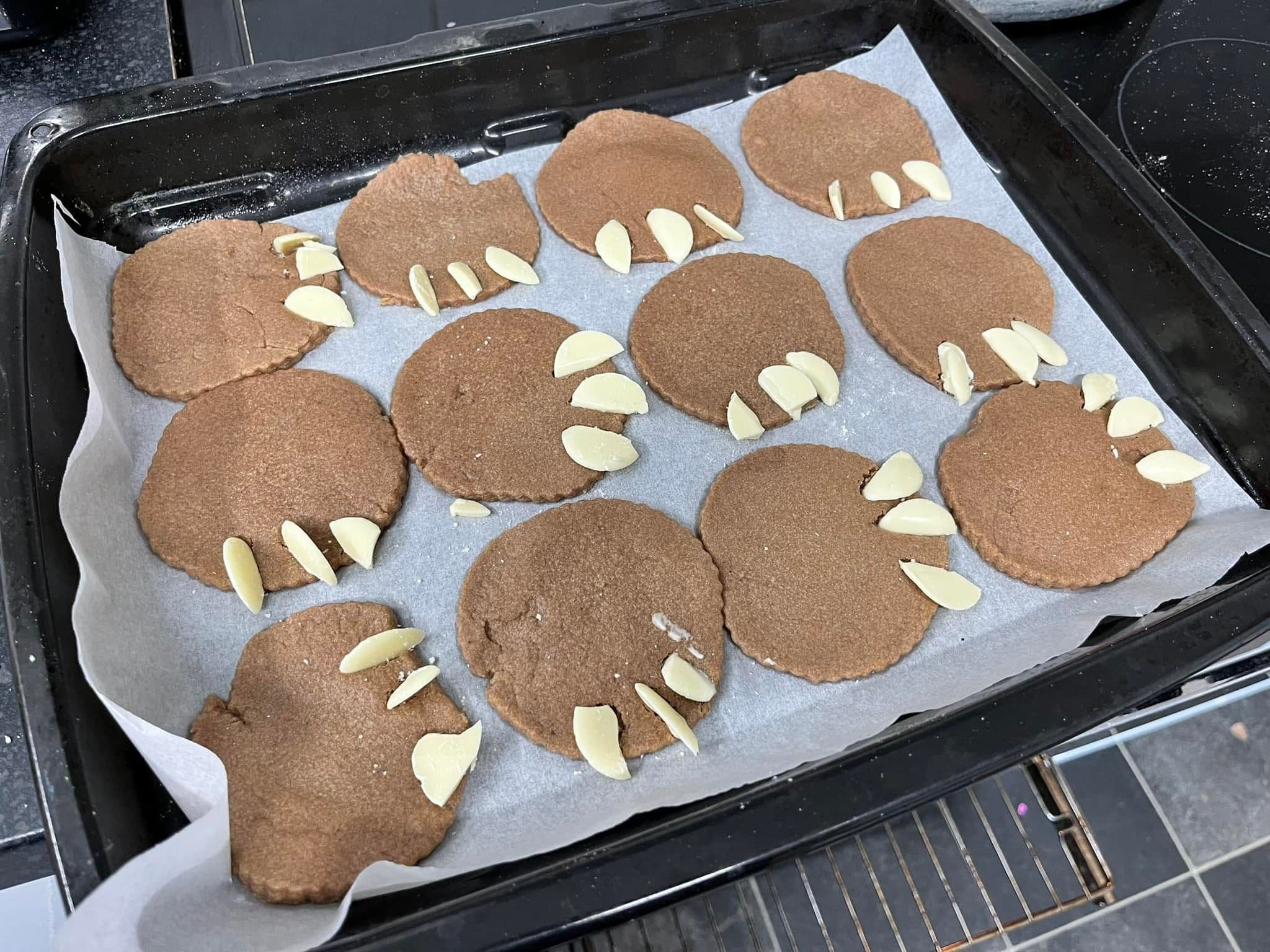 A baking tray of home-made dinosaur-footprint biscuits decorated with flaked almond claws.