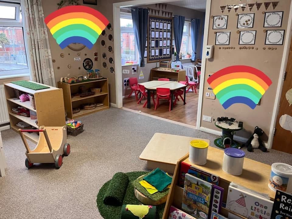 A bright nursery playroom with large painted rainbows on the wall, low tables with red chairs and shelves of toys.
